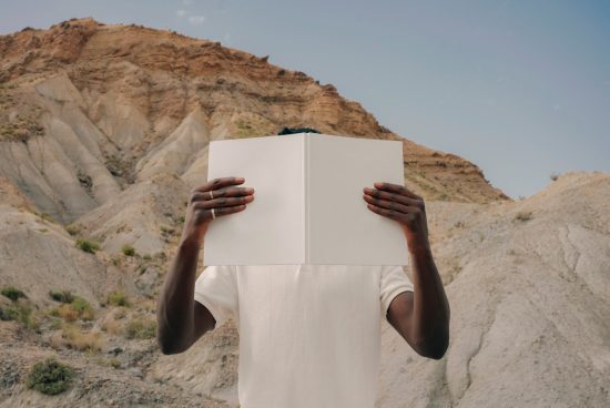 Person holding blank open book mockup against natural rocky background, ideal for presentations, graphic design assets.